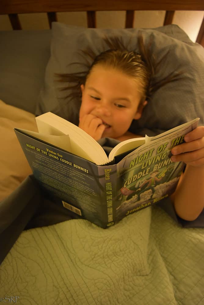 Little girl reading scary book in bed