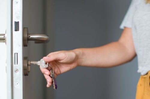 A woman with her hand on a key that is inside her front door's locking mechanism.