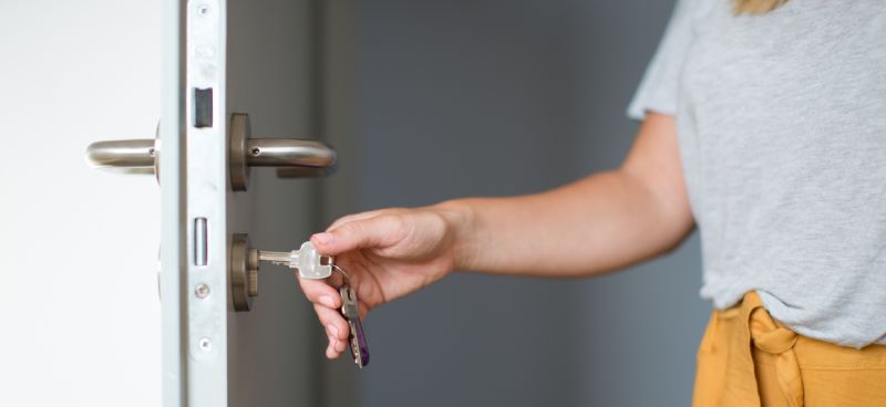 A woman with her hand on a key that is inside her front door's locking mechanism.