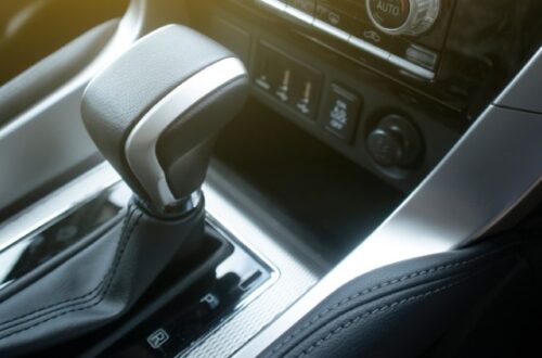 The shifter of a car sits in park. The sunlight shines into the window, highlighting the radio and AC controls.