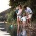 A young couple with two young children standing by a river while holding sticks made to look like fishing poles.