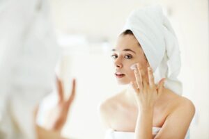 Pretty girl applying moisturizing cream in front of mirror