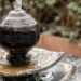 A small three-tiered fountain in a backyard. The round stone on top dribbles water down onto the tray-like lower tiers.