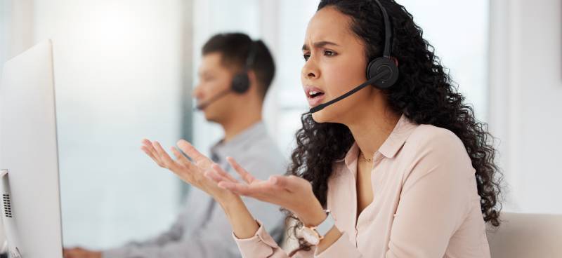 A woman with an exasperated expression gesturing with two open palms to her monitor. She is wearing a headset. Tax Professionals