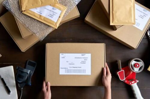 A dark wooden table displays various shipping materials, like bubble wrap, padded mailers, and cardboard boxes.