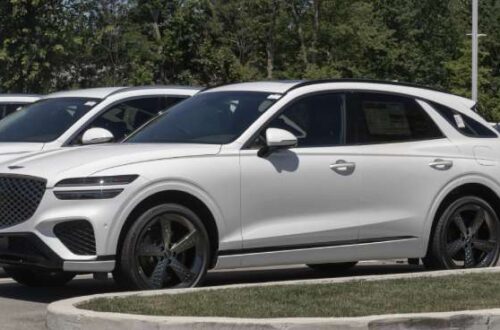 A new Genesis GV70 Sport stock turbocharged SUV is parked in a dealership lot surrounded by similar vehicles.