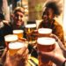 A group of four friends holding up their beers, celebrating while sitting in the outdoor area of a brewery.