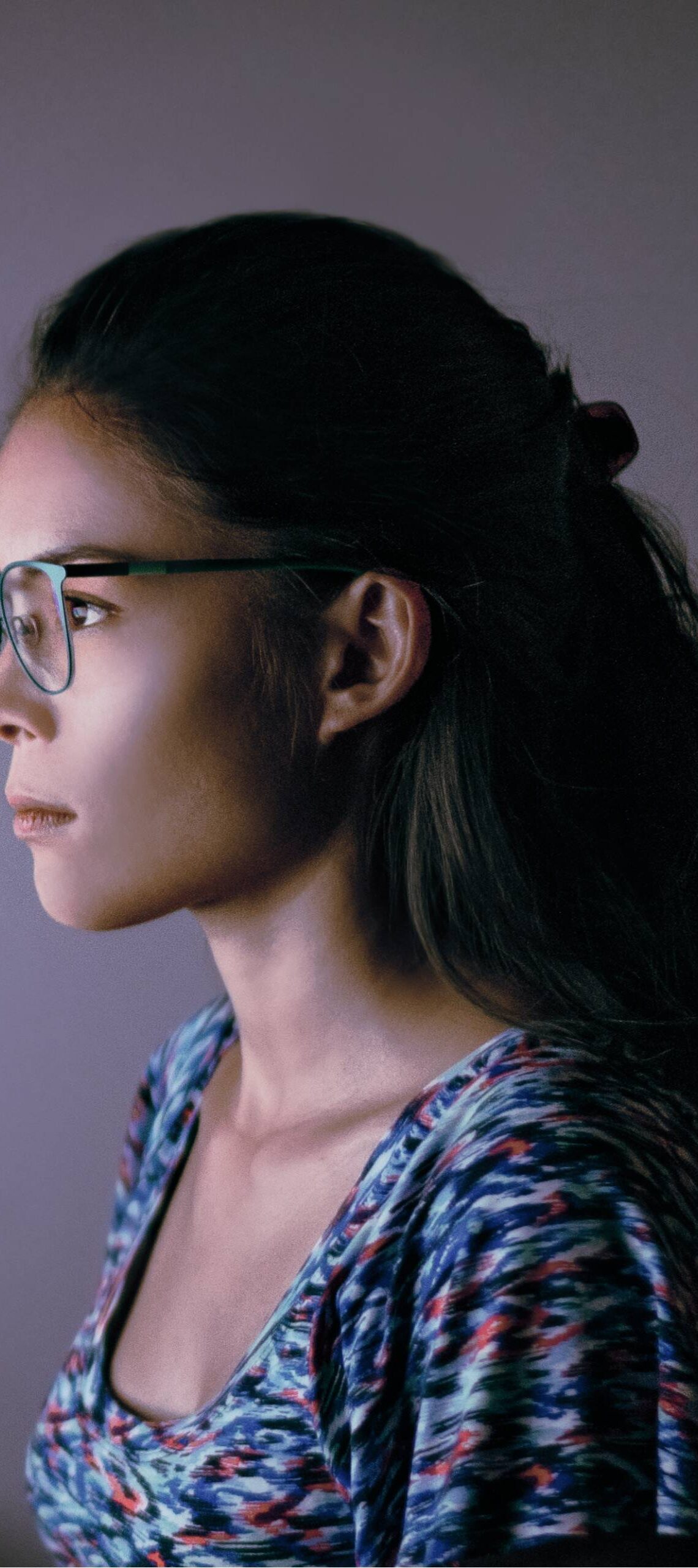 A female remote worker sitting at her desk wearing a pair of blue light glasses in front of her computer monitor.