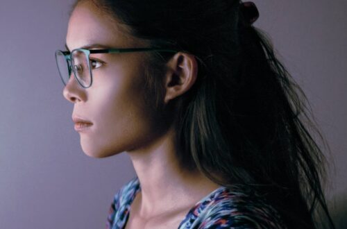 A female remote worker sitting at her desk wearing a pair of blue light glasses in front of her computer monitor.