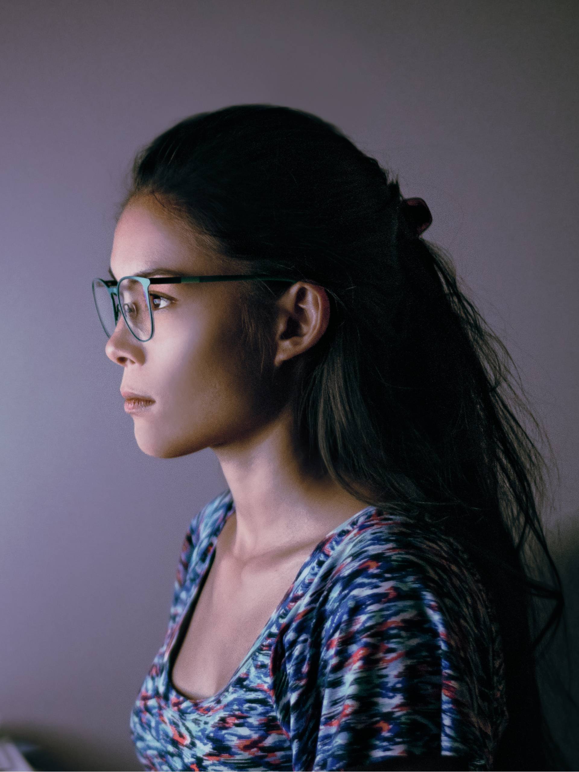 A female remote worker sitting at her desk wearing a pair of blue light glasses in front of her computer monitor.