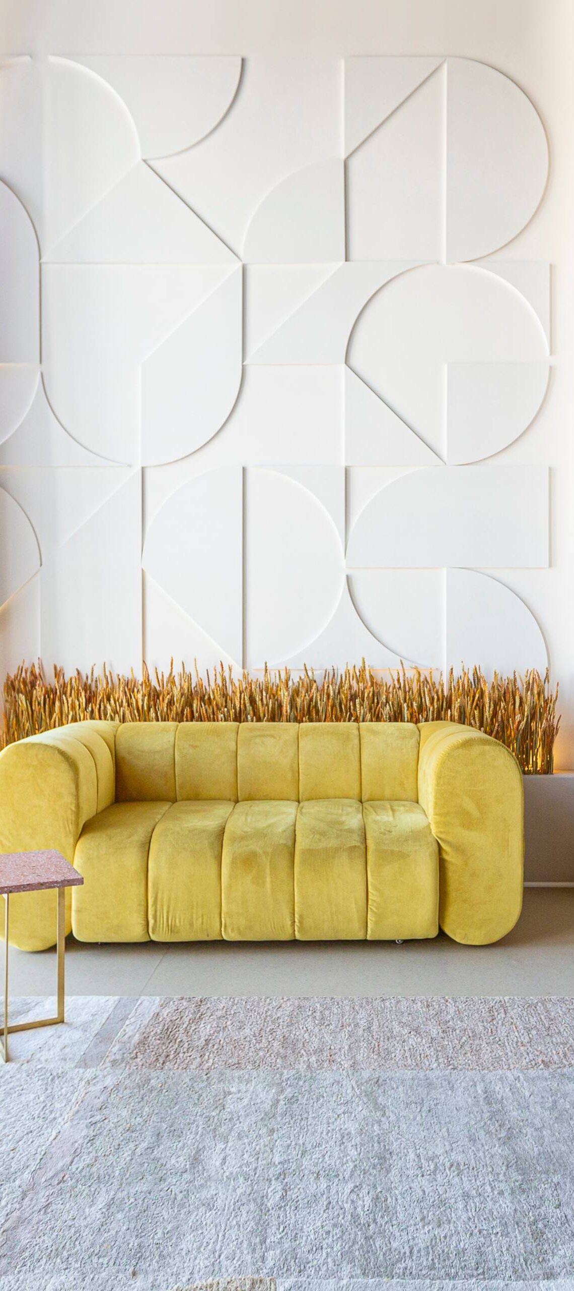 A modern loft apartment with large floor-to-ceiling windows, a yellow couch, and eccentric wall decor to the right.