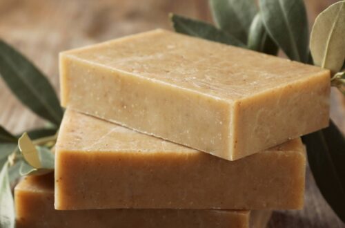 A stack of three homemade soap bars sitting on a wooden table. There's an olive branch and a few olives next to the stack.