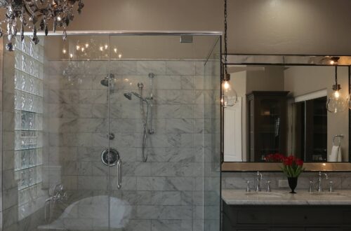 An updated bathroom with a chandelier hanging over the jacuzzi tub and warm pendant lights over the vanity.