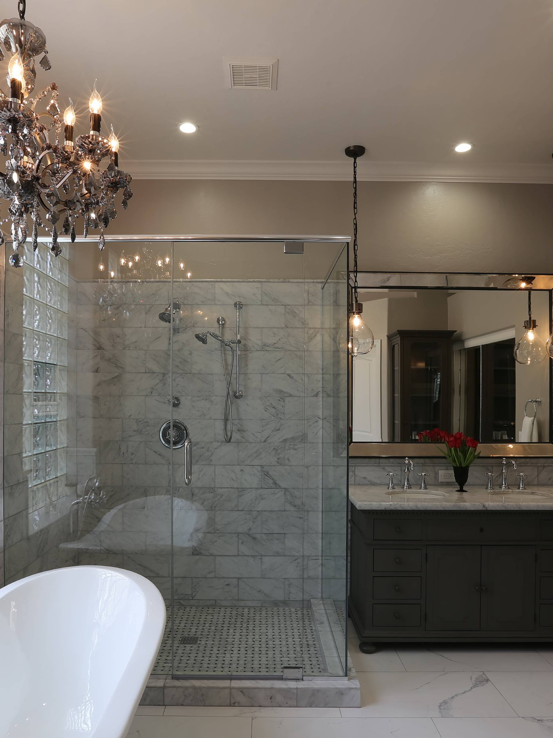 An updated bathroom with a chandelier hanging over the jacuzzi tub and warm pendant lights over the vanity.