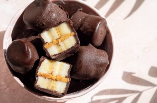 A bowl of dark chocolate-covered piece of banana on a table with a light shining through to create shadows of plants.