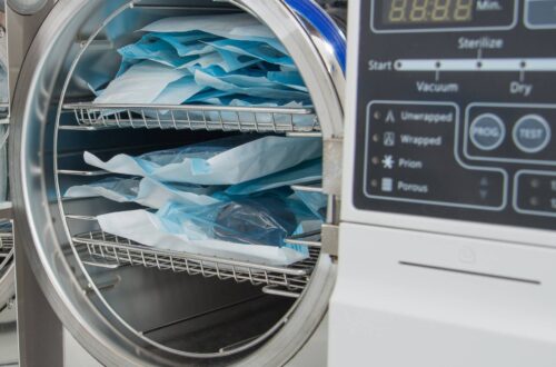 A laboratory autoclave with the door open. There is a tray inside the sterilizer that's full of surgical instruments.