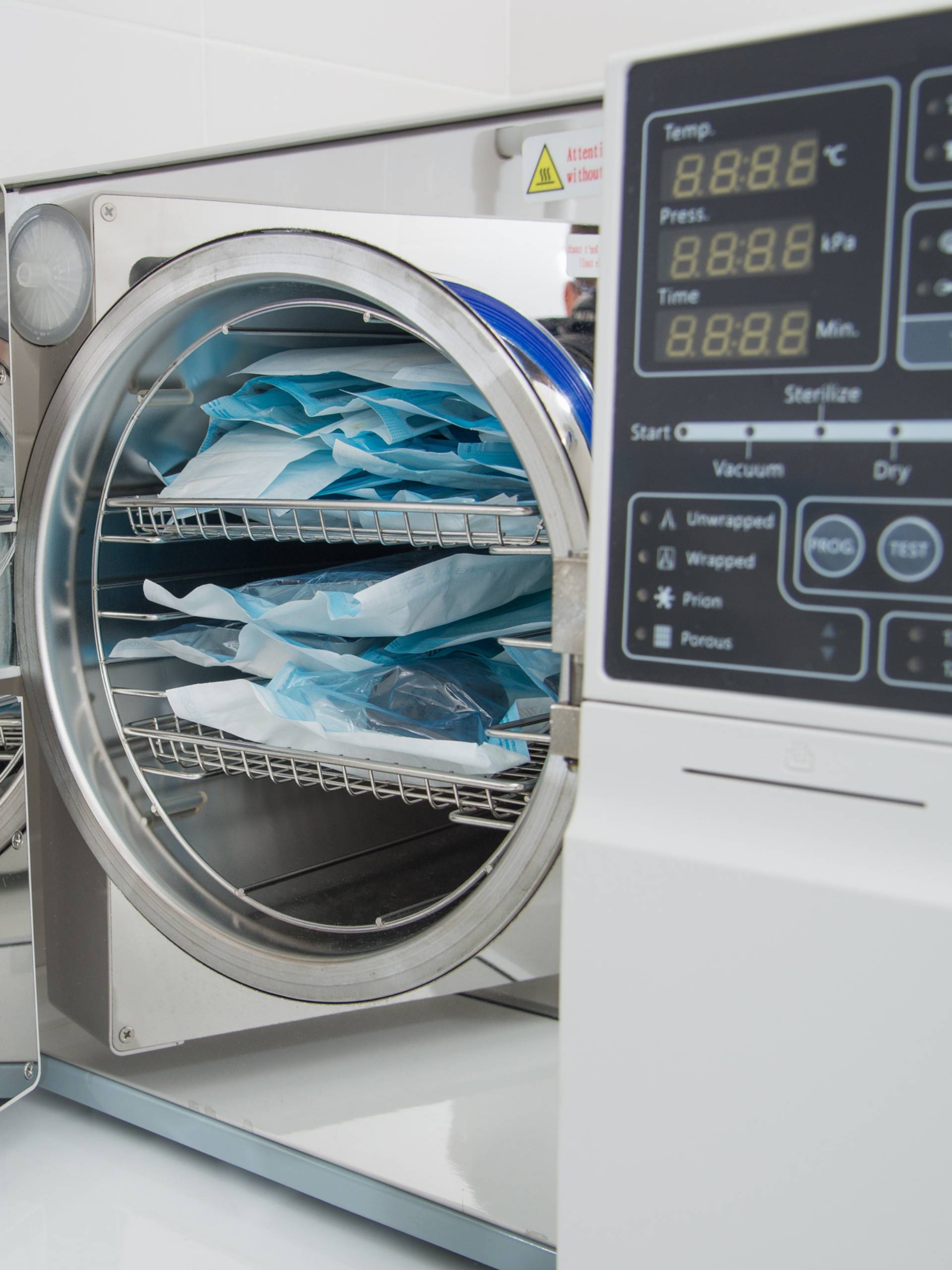 A laboratory autoclave with the door open. There is a tray inside the sterilizer that's full of surgical instruments.