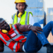 A Black male engineer is injured and on the ground, while a Black female engineer looks at his injury on his shin.