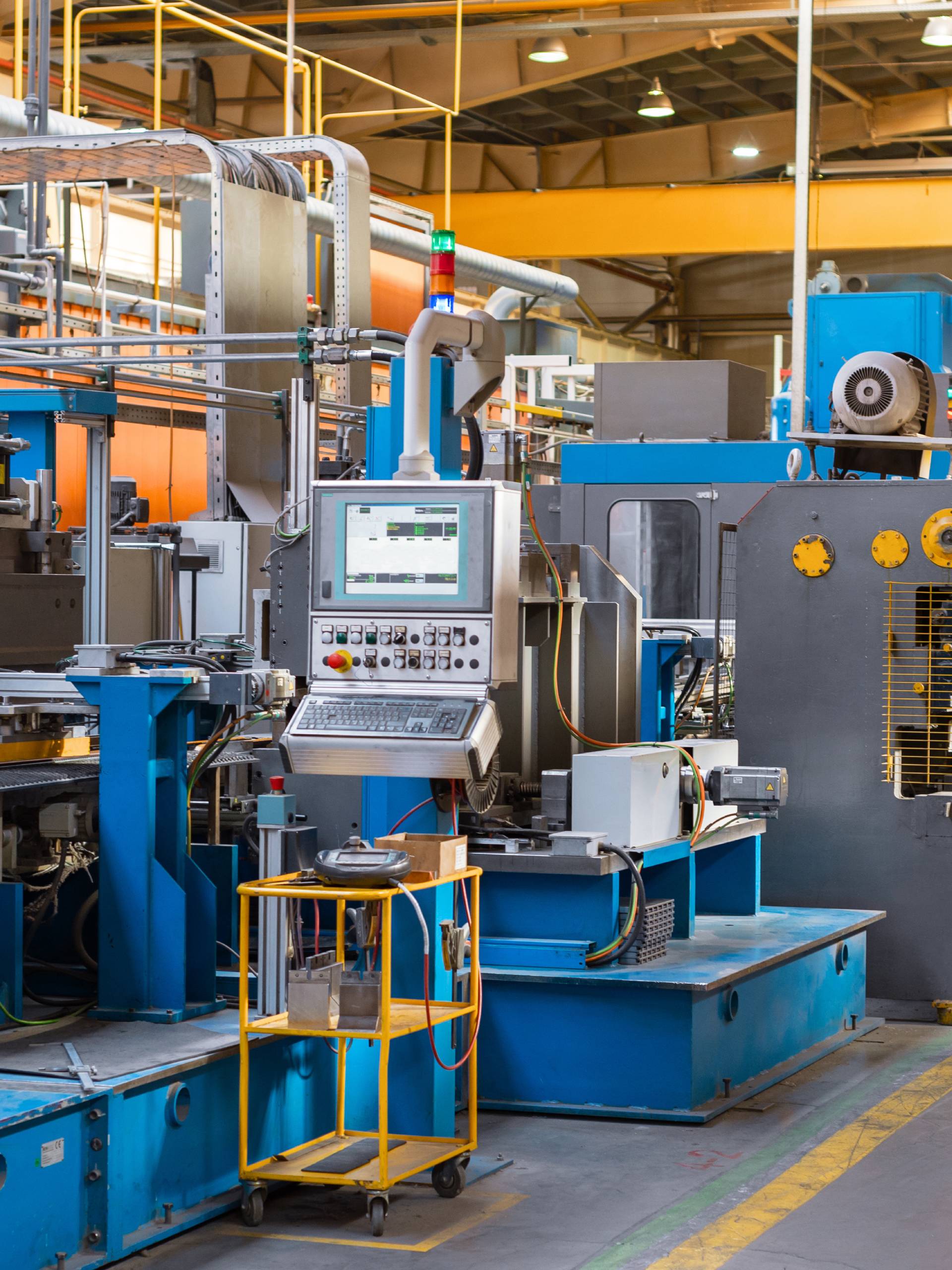 An industrial warehouse with various types of equipment installed. There are yellow hazard lines and scaffolding above.