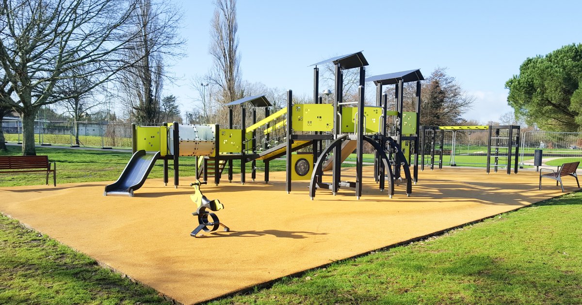 A newly installed playground with no children playing. It's sunny outside and the gym equipment is black and lime green.