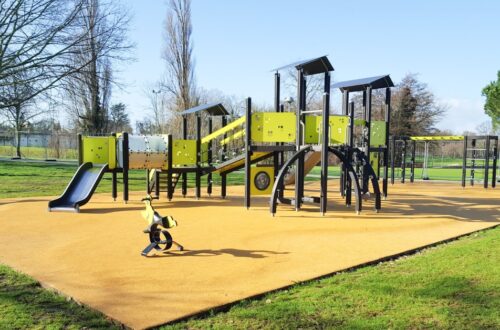 A newly installed playground with no children playing. It's sunny outside and the gym equipment is black and lime green.