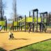 A newly installed playground with no children playing. It's sunny outside and the gym equipment is black and lime green.