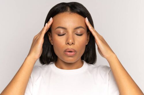 A woman wearing a white shirt in front of a white background holding her hands up to her forehead as she tries to destress.