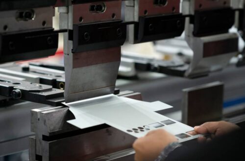 An operator holding a sheet of metal near a sheet bending machine, after the metal has been stamped.