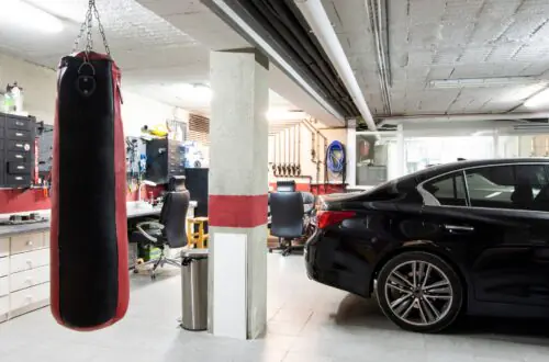 A black sedan and a white car are parked inside a garage with cabinetry, a punching bag, and tile flooring visible.