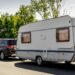 A caravan trailer on a freeway road. A Black SUV is carrying the caravan on the highway near a ramp.