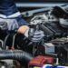 A professional mechanic is working on a vehicle and is wearing robust gloves. Theyr'e working on the engine.