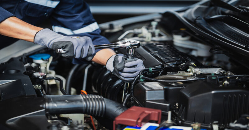 A professional mechanic is working on a vehicle and is wearing robust gloves. Theyr'e working on the engine.
