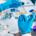 A close-up of a scientist wearing a white coat and blue gloves testing a substance in a beaker and swishing it around.