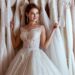 A woman in a wedding dress with a lace bodice and A-line skirt leans against a rack filled with countless wedding gowns.
