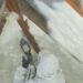 A contractor wearing a white protective suit applies spray foam insulation to the ceiling of an attic.