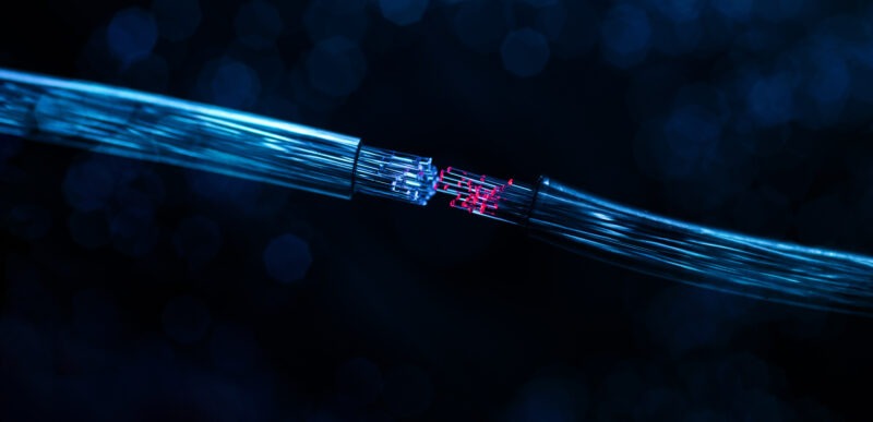 Two clear fiber optic tubes coming together. Inside are blue and red cables coming together to form a connection.