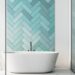 A modern bathroom with a white standalone tub, turquoise tiles, and a white bench. On the bench are bottles and a plant.