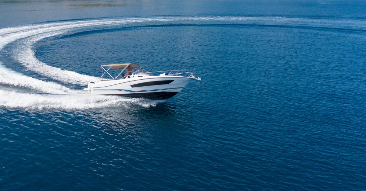 An aerial view of a luxury speed boat on the ocean making a sharp turn in the water. The boat created a curved wake.