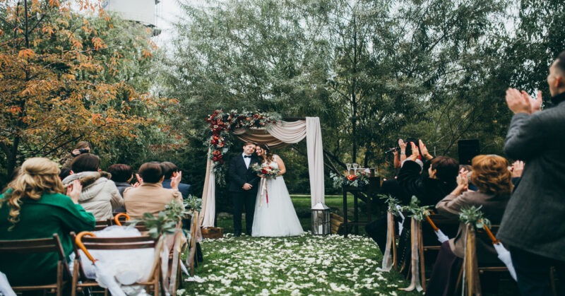 A beautiful fall wedding ceremony with chairs on the aisle, and a couple stands at the altar with flower petals in the aisle.