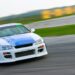 A white race car with a blue stripe and orange details skids along a track, the background blurred from speed.
