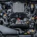 An overhead view of the engine of a black car. The image is well-lit, with the area around the car being dark.