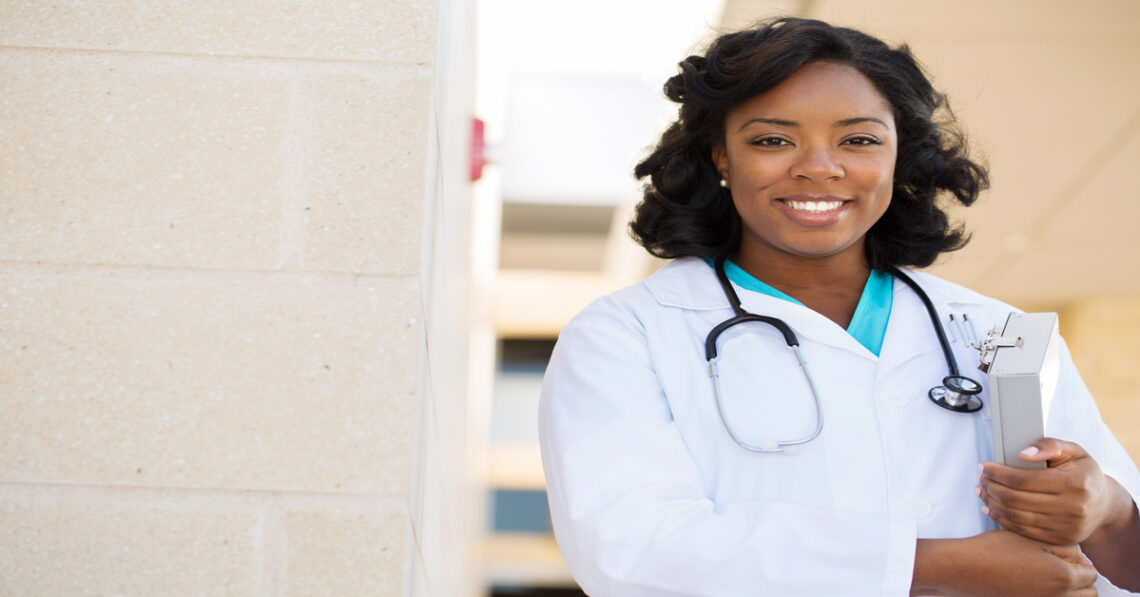 Urgent Care A Black woman wearing a doctor's coat and a stethoscope around her neck smiles widely. She is holding a clipboard. Urgent care post