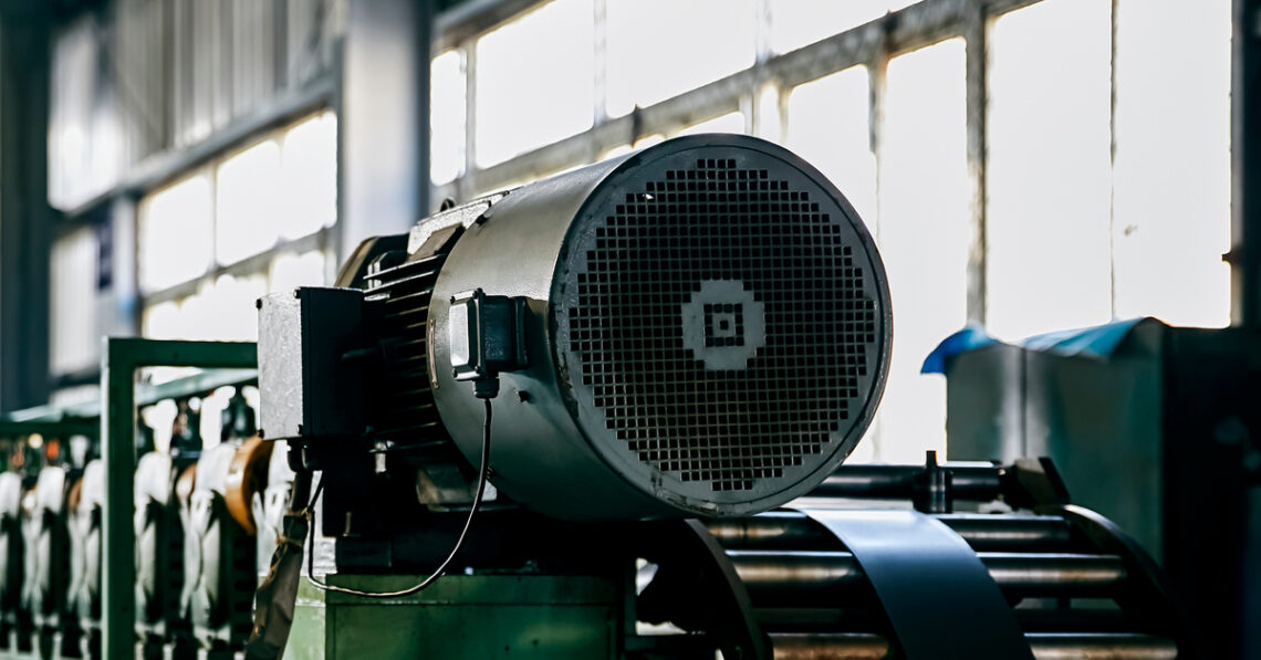 An industrial machine that is dirty and a bit outdated. The machine is sitting in front of a long set of windows.