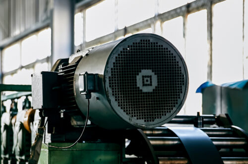 An industrial machine that is dirty and a bit outdated. The machine is sitting in front of a long set of windows.