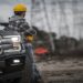 A man in a hard hat is leaning against his car as he’s looking off into the distance at several electrical towers.