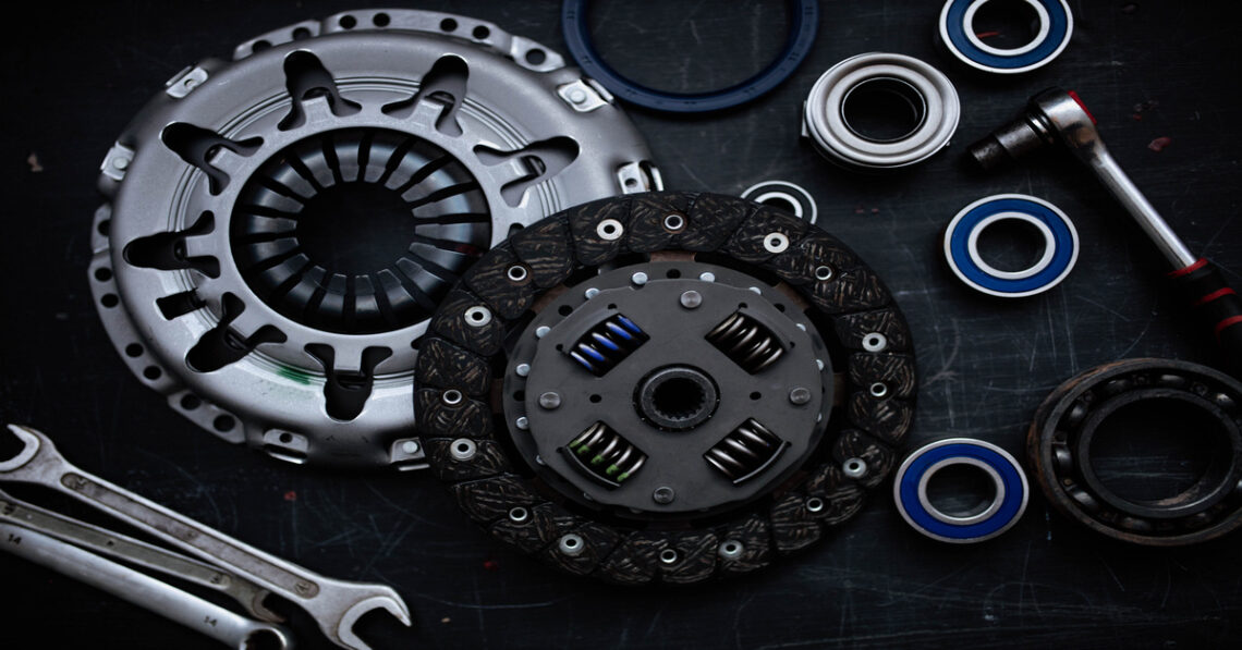 An overhead view of a new automotive clutch kit on a black table, including a flywheel, bearings, rings, and wrenches.