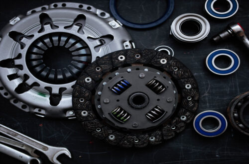 An overhead view of a new automotive clutch kit on a black table, including a flywheel, bearings, rings, and wrenches.