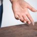 A thin layer of dust is on a wooden table. A person has dust on their fingertip after they swiped the dusty surface.