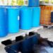 A warehouse with blue drums sitting against the wall and a black spill on the ground surrounding the blue drums.