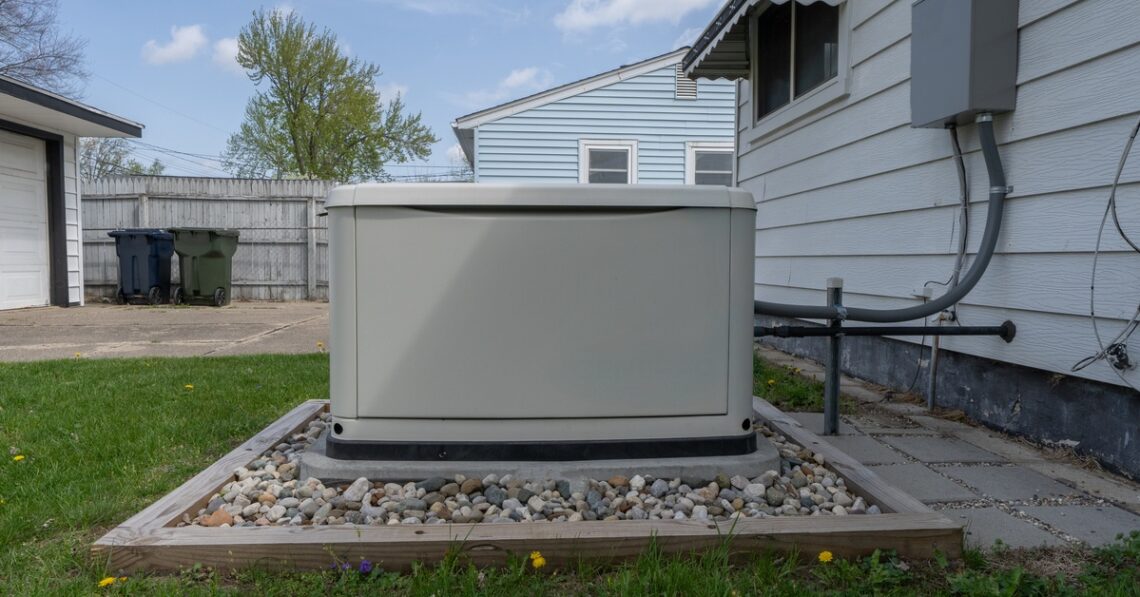 A backup power generator sits on a bed of decorative stones on a lawn outside of a residential home.